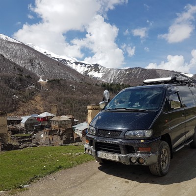 4x4 busje tijdens dagtocht naar Ushguli, met Svaneti-torens en besneeuwde Kaukasusbergen op de achtergrond.