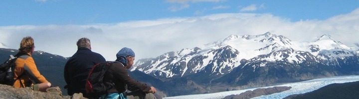 Wandelaars kijken uit over een gletsjer en besneeuwde bergen.
