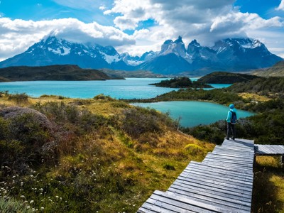 Wandelaar op vlonderpad met uitzicht op turquoise meren en de Torres del Paine-bergen in Patagonië.