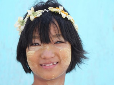 Portret van een meisje in Myanmar met thanaka op haar gezicht en een bloemenkrans in het haar.