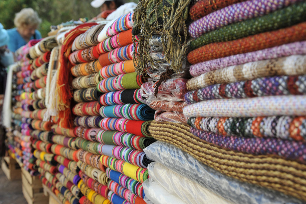 Kleurrijke stapels geweven dekens en textiel op een markt tijdens een groepsrondreis door Argentinië.