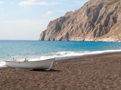 Witte boot op zwart zandstrand met rotsachtige kust en blauwe zee op Santorini, Griekenland.