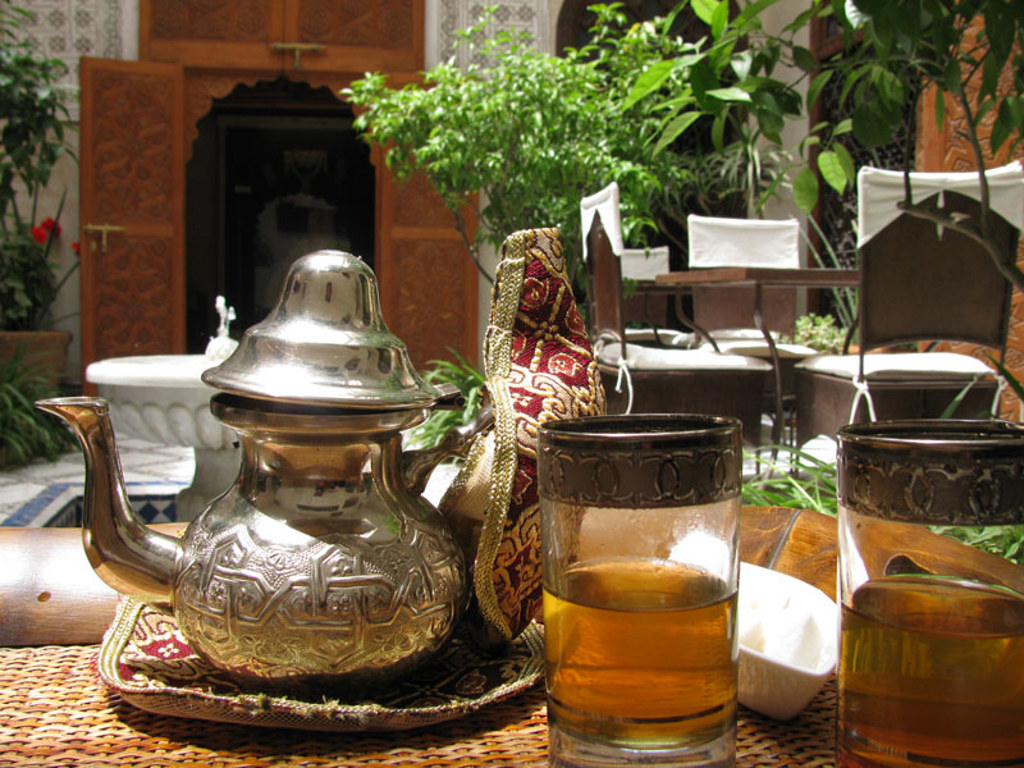 Marokkaanse muntthee in zilveren theepot en glazen op tafel in een riad-binnenplaats.