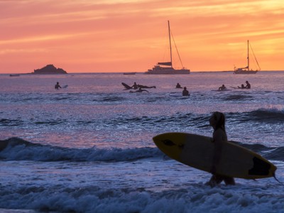 Surfers en zeilboten bij zonsondergang aan de kust van Costa Rica.