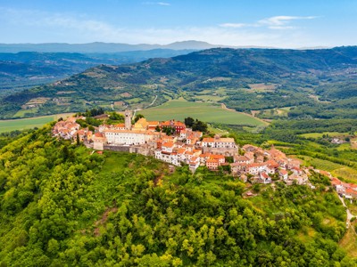Panoramisch uitzicht op een heuveldorp met rood-oranje daken en kerktoren, omringd door groene valleien in Italië.