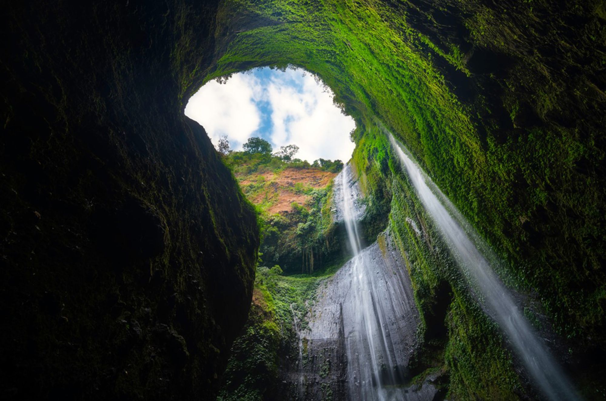 Waterval stroomt door een groene grot met opening naar de lucht in Indonesië.