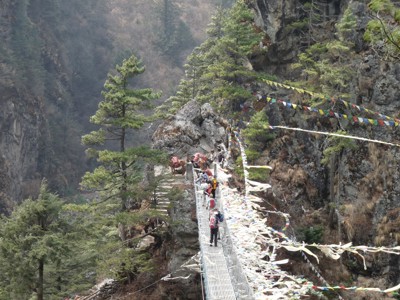 Wandelaars steken hangbrug met gebedsvlaggen over tijdens de Route Nepal Everest Base Camp.