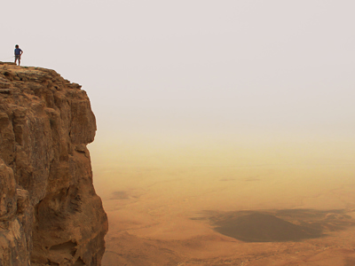 Wandelaars op een rotsklif met uitzicht over de uitgestrekte woestijn in Jordanië.