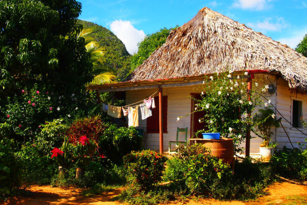 Casas particulares in Cuba met rieten dak, veranda en tropische tuin bij groene heuvels.