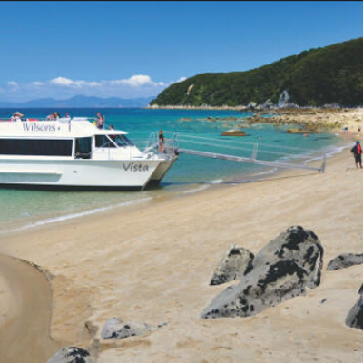 Cruiseboot bij strand in Abel Tasman National Park, met wandelaars langs de kust.
