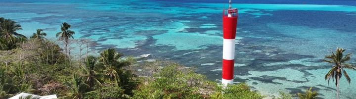 Rood-witte vuurtoren aan de kust van San Andres, met palmbomen en turquoise zee.