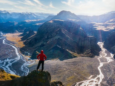 Wandelaar kijkt uit over berglandschap en rivierdelta langs de Laugavegur Trail in IJsland.
