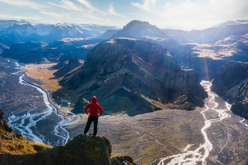 Wandelaar kijkt uit over berglandschap en rivierdelta langs de Laugavegur Trail in IJsland.