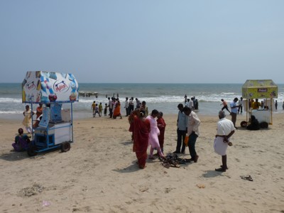 Strand in Zuid-India met mensen bij de branding en snackkarren op het zand.