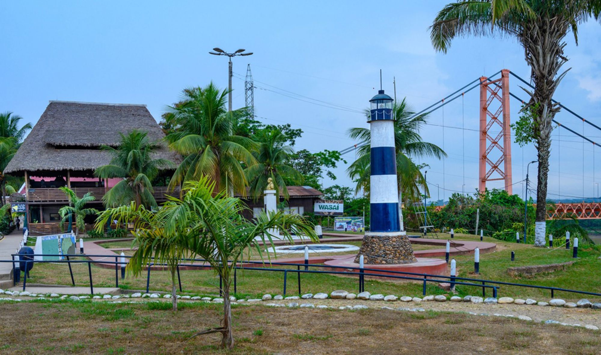 Blauw-witte vuurtoren in een park met palmbomen en hangbrug op de achtergrond in Peru.