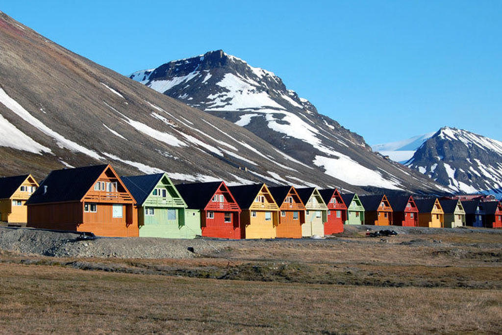 Gekleurde houten huisjes in Longyearbyen op Spitsbergen, met besneeuwde bergen op de achtergrond.