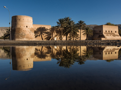 Fort met palmbomen, weerspiegeld in het water langs de route Oman en Dubai.