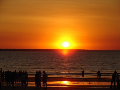 Zonsondergang boven zee aan de kust van West-Australië, met silhouetten van mensen op het strand.