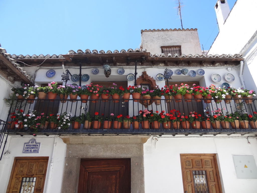 Wit Andalusisch huis met balkon vol bloempotten en blauw-wit aardewerk, tijdens een 22-35ers reis door Andalusië.