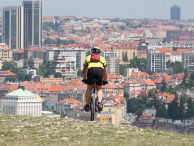 Fietser met rugzak kijkt uit over de skyline en daken van Praag tijdens de fietsreis van Praag naar Wenen.