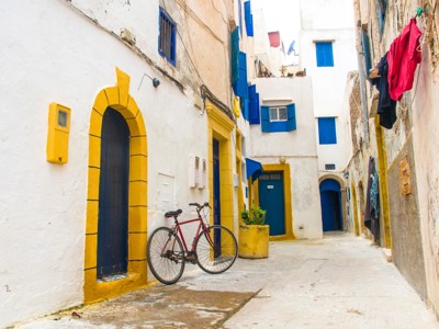 Smalle straat in Essaouira met witgekalkte huizen, blauwe deuren en een fiets tegen de muur.