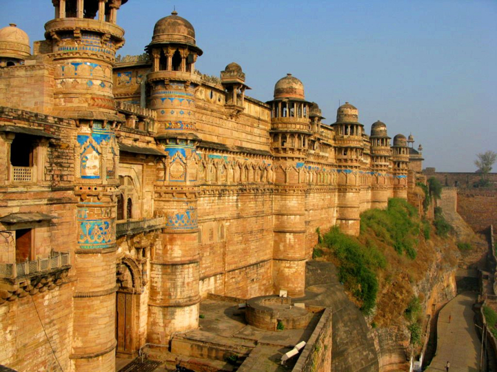 Fort Gwalior in India met zandstenen muren, koepels en blauwe mozaïeken boven een ravijn.