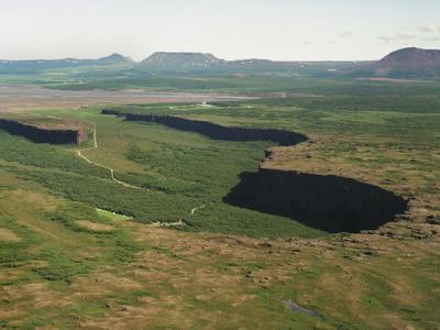 Uitzicht over de breuklijn van Þingvellir Nationaal Park in IJsland, met groene vlaktes en kliffen.