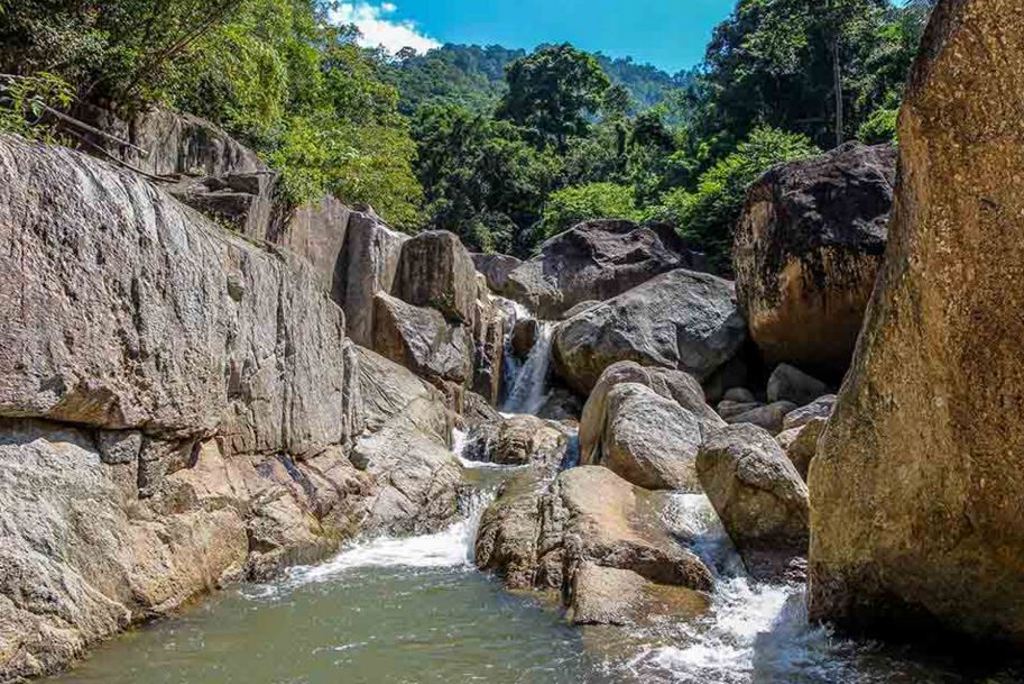 Waterval tussen grote rotsblokken in een groene jungle in Thailand, tijdens de rondreis Thailand Chill & Adventure.
