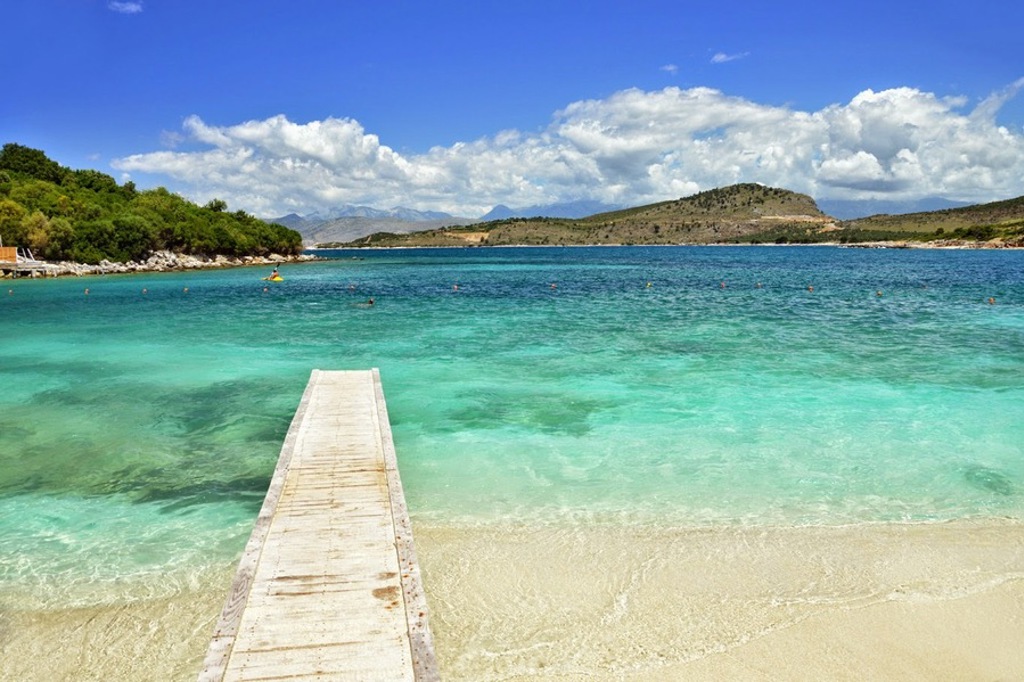 Houten steiger naar een helderblauwe baai aan de Albanese kust, tijdens een 22-35ers reis Albanië.