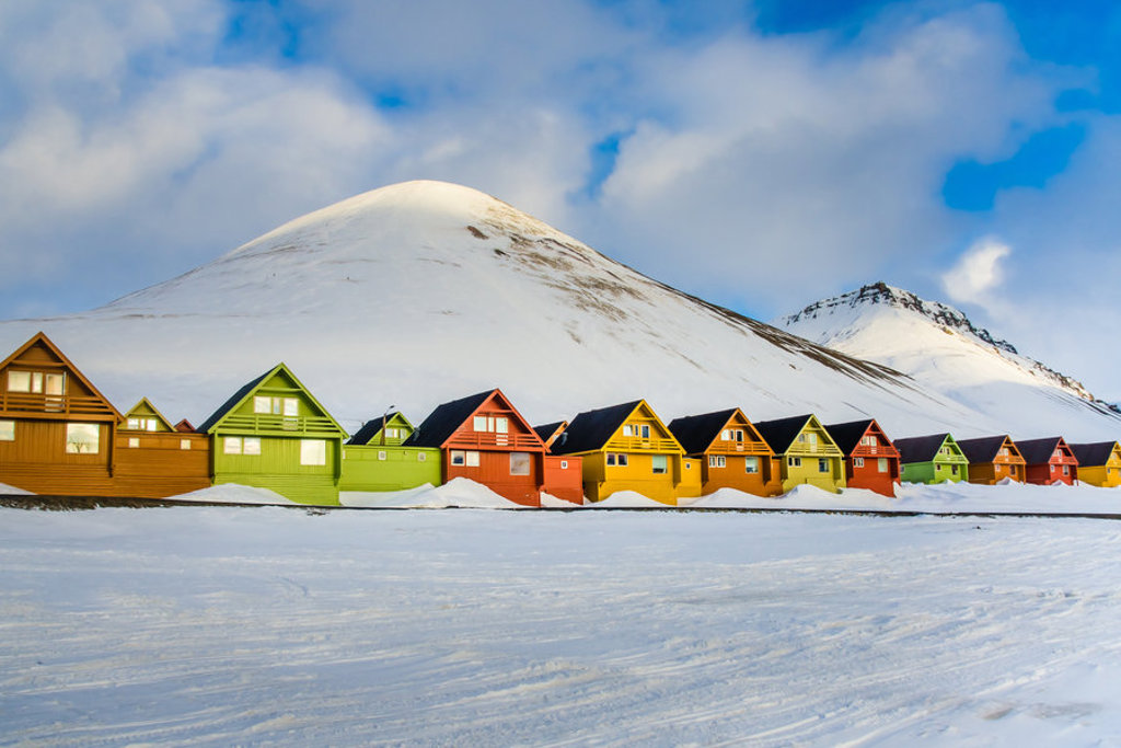 Kleurrijke houten huizen in Longyearbyen op Spitsbergen, met besneeuwde bergen op de achtergrond.