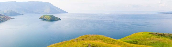 Panoramisch uitzicht over het Tobameer op Sumatra, met groene heuvels en helderblauw water.