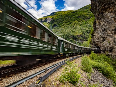 Groene trein rijdt door een bergachtig landschap langs een rotswand in Scandinavië.