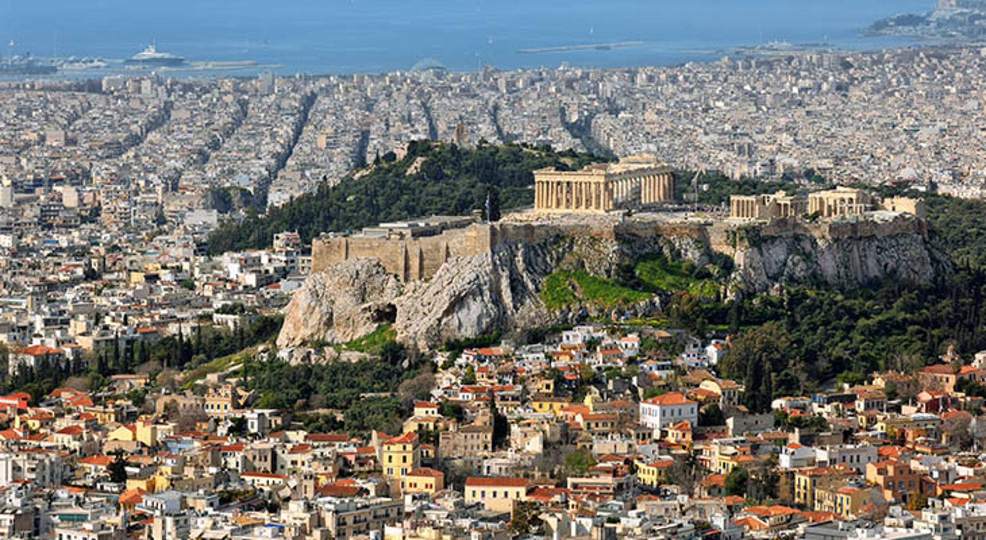 De mooiste stad ter wereld Athene Uitzicht op de Akropolis met het Parthenon boven Athene en de kustlijn op de achtergrond.