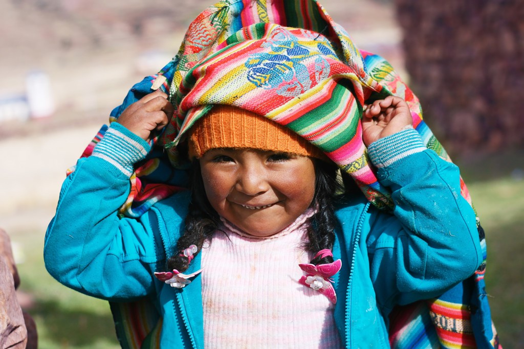 Lachend meisje in Peru met kleurrijke doek en muts tijdens een rondreis.