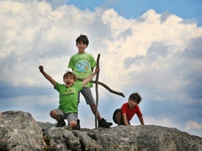 Kinderen poseren op een rots met wandelstok tijdens familiereis in de Écrins, Frankrijk.