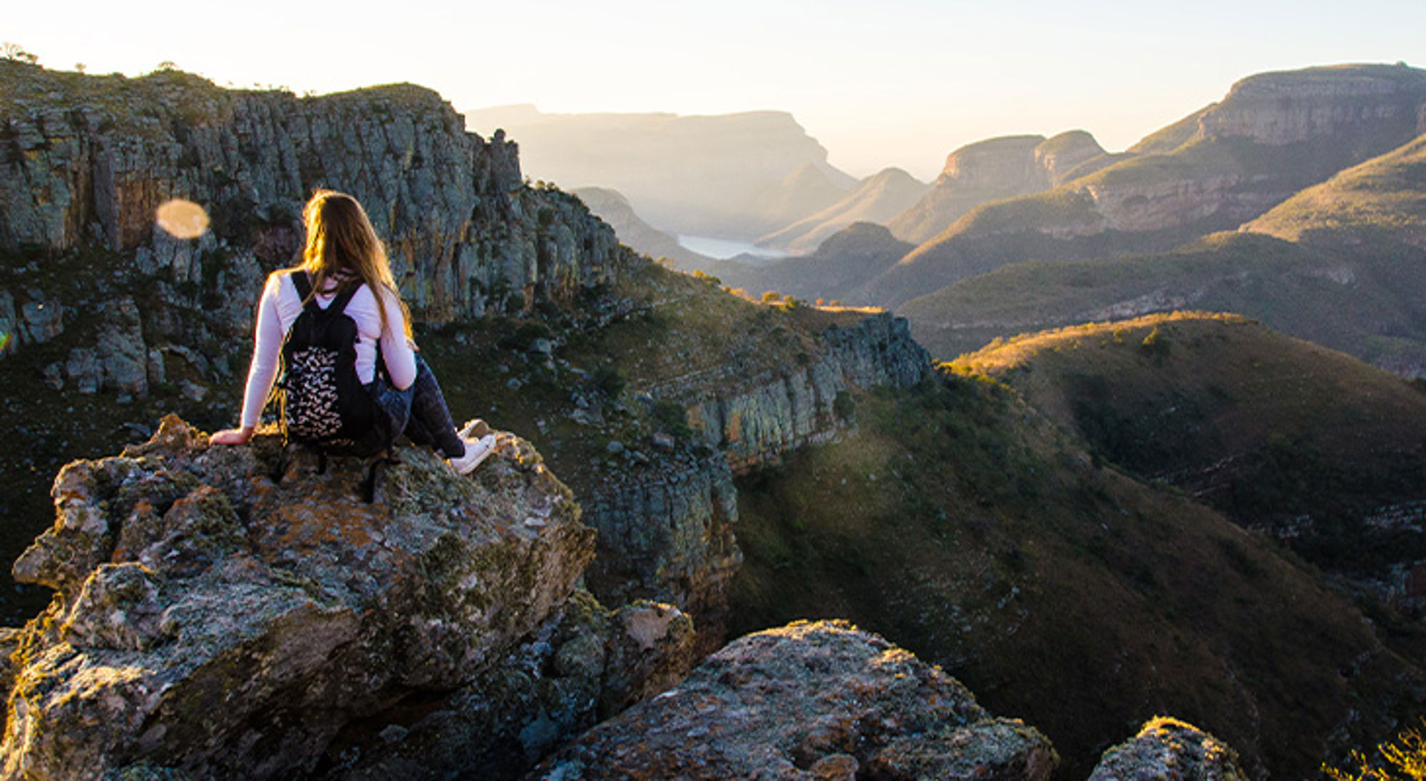 Blyde River Canyon Zuid-Afrika Vrouw met rugzak zit op een rots en kijkt uit over een berglandschap bij zonsondergang.