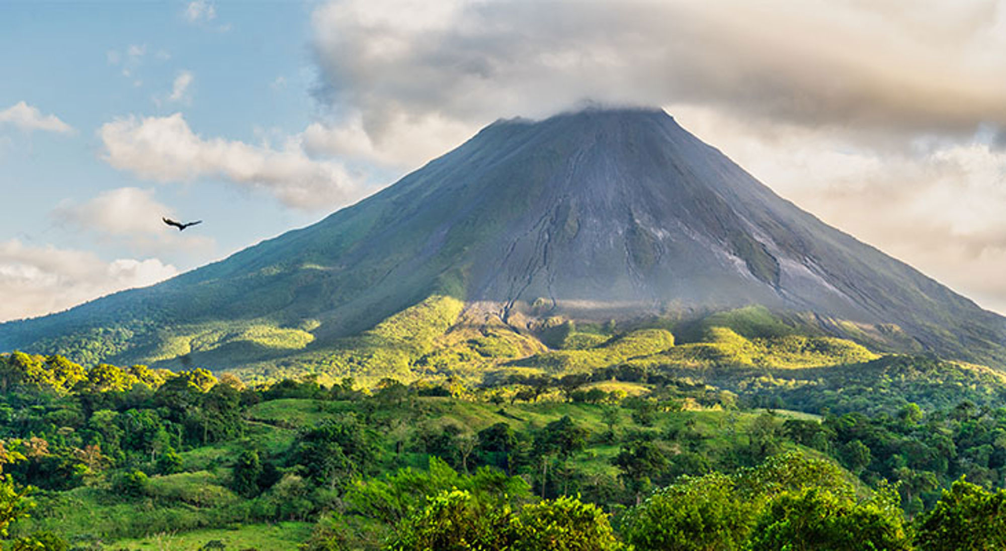 El Arenal vulkaan Arenal-vulkaan in Costa Rica boven groen regenwoud en heuvels onder een bewolkte lucht.