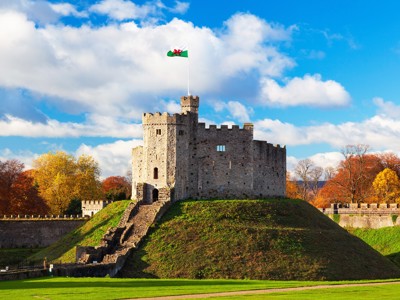 Kasteel van Cardiff met Welshe vlag, omringd door herfstbomen onder een blauwe lucht.