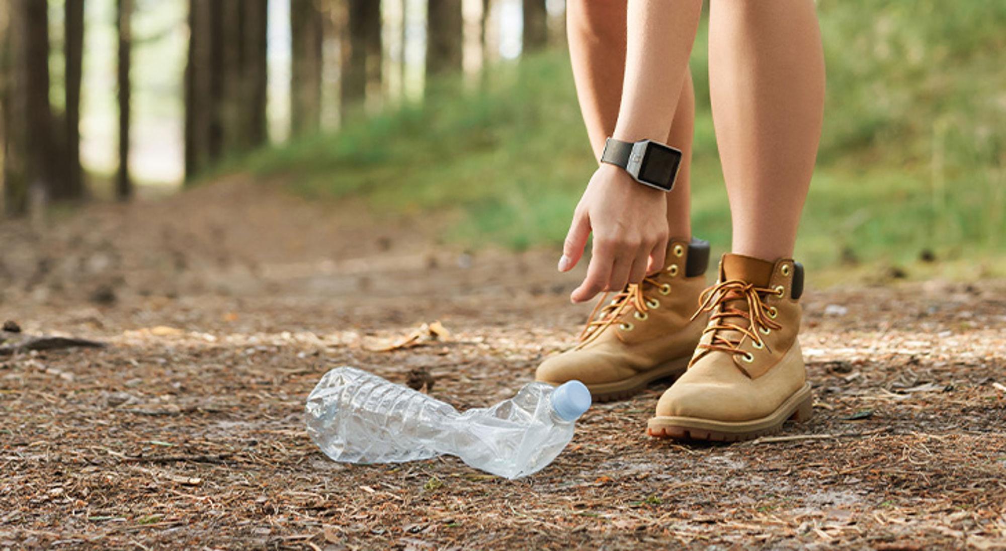 Transhpacking Wandelaar raapt een plastic fles op van het bospad tijdens een wandeling.