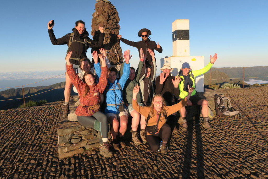 Wandelaars poseren juichend op een bergtop op Madeira, bij een geodetisch monument.