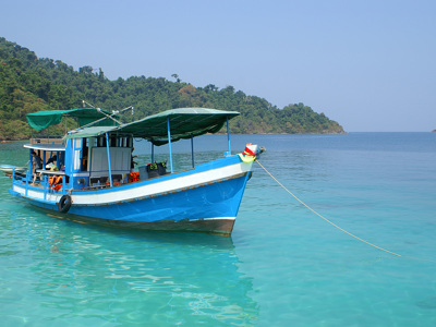 Blauwe boot in helder turquoise water bij een groen eiland in Thailand.