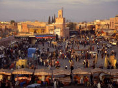 Drukke Jemaa el-Fna in Marrakech bij zonsondergang, met kraampjes en de Koutoubia-moskee op de achtergrond.