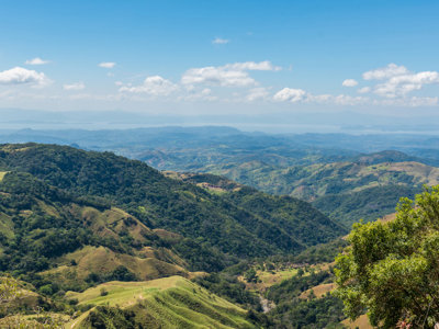 Panoramisch uitzicht op groene berglandschappen in Costa Rica onder een blauwe lucht met wolken.