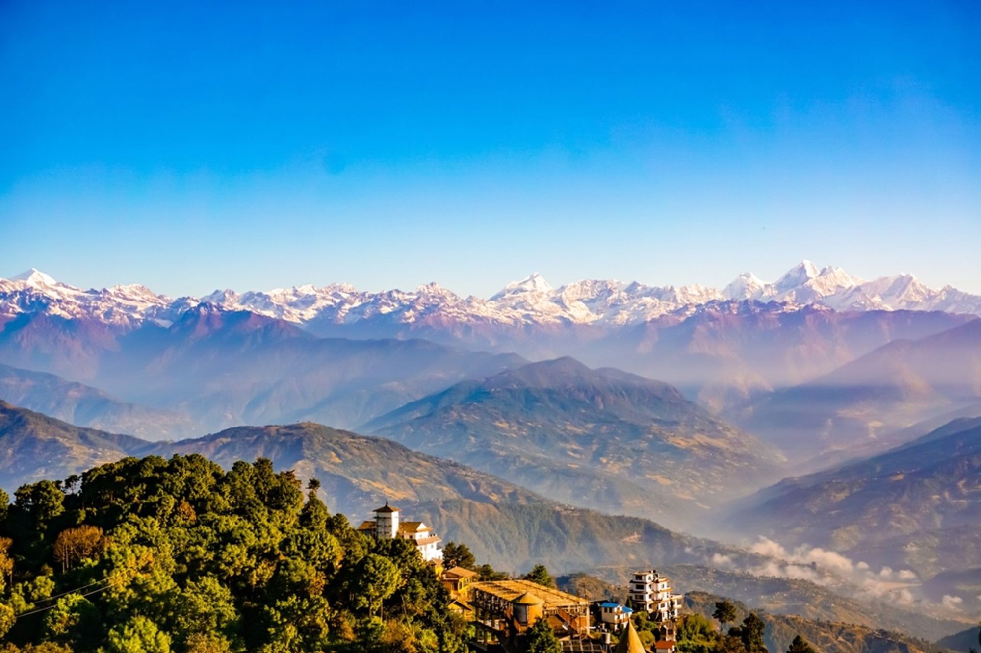 Uitzicht op de Himalaya met besneeuwde bergtoppen en dorp op een groene heuvel in Nepal.