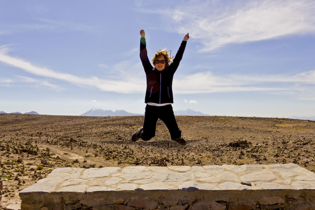 Vrouw springt juichend in de lucht tijdens rondreis door Peru, met berglandschap op de achtergrond.