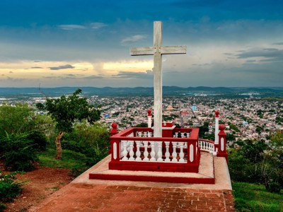 Uitzicht vanaf El Cobre op Santiago de Cuba met kruis op het uitkijkpunt bij zonsondergang.