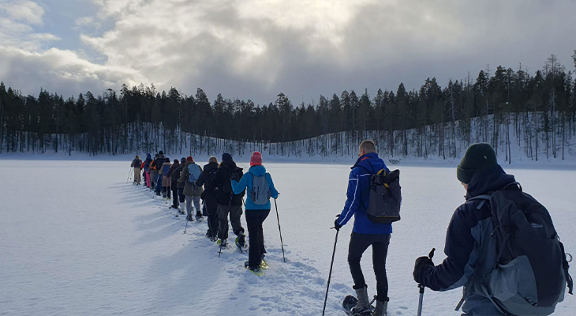 Sneeuwschoenen Finland Groep wandelaars met sneeuwschoenen trekt over een bevroren meer richting het bos.