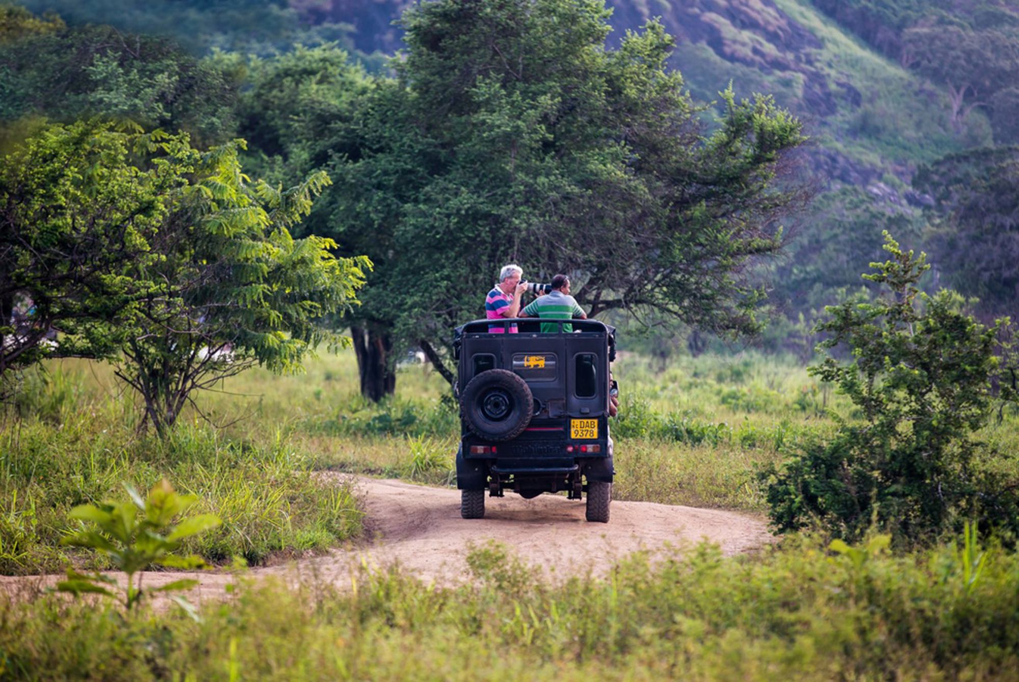 Safari-jeep met reizigers op onverharde weg door groen landschap in Sri Lanka.