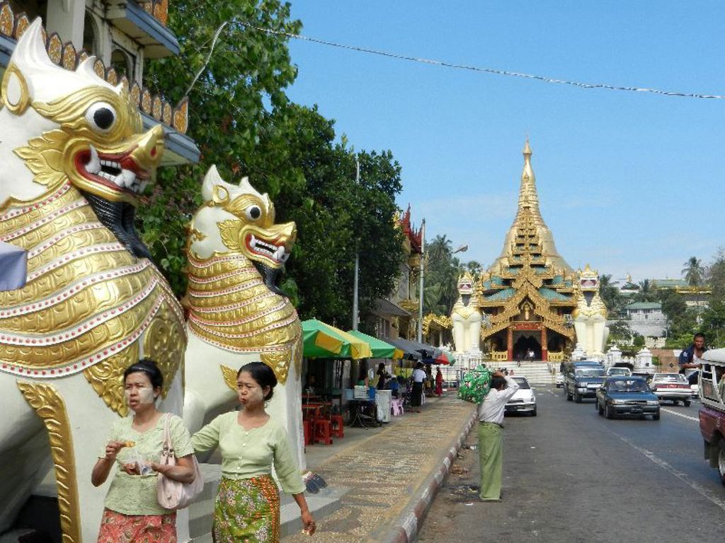 Gouden tempel met leeuwenbeelden bij ingang in Myanmar, langs een drukke straat.