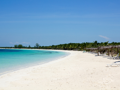 Wit zandstrand in Cuba met turquoise zee, palmbomen en rieten parasols met ligbedden.